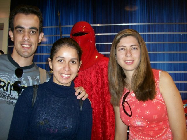 Da esquerda para direita: Meu irmão da minha amiga, minha amiga e eu. Foto da cintura para cima dentro da loja do Star Wars, aarece a cabeça de algum boneco atrás de nós.