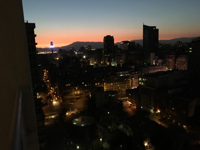 A foto foi tirada na varanda do apartamento, mostra parte da cidade de Santiago com o pôr do sol