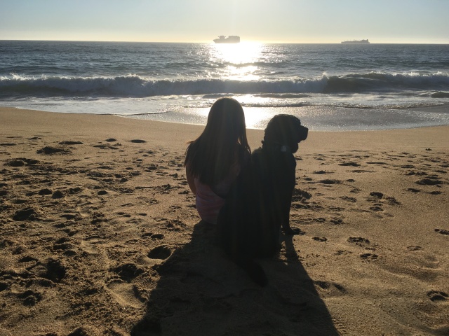 Eu e Hilary estamos sentadas de costas para foto apreciando o mar, Hilary está olhando para direita